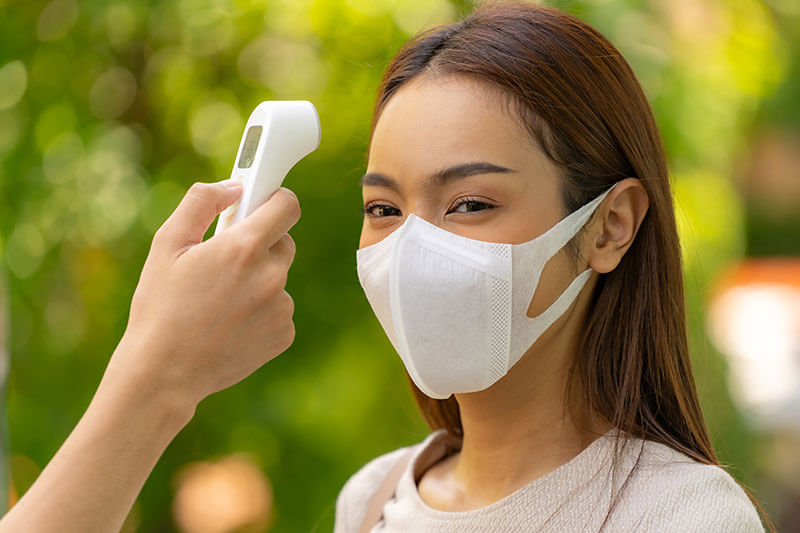 taking temperature of woman wearing face mask